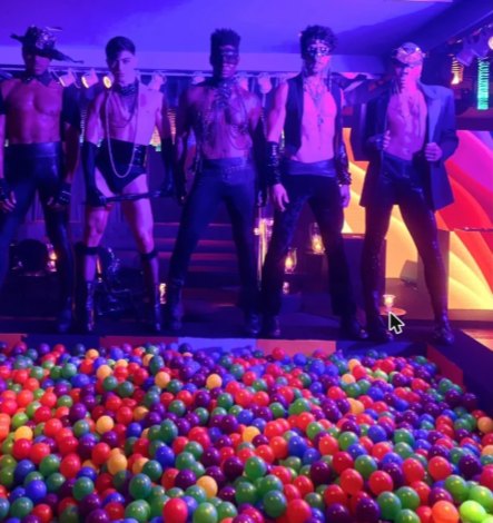 Performers enmascarados sobre un escenario con piscina de bolas de colores