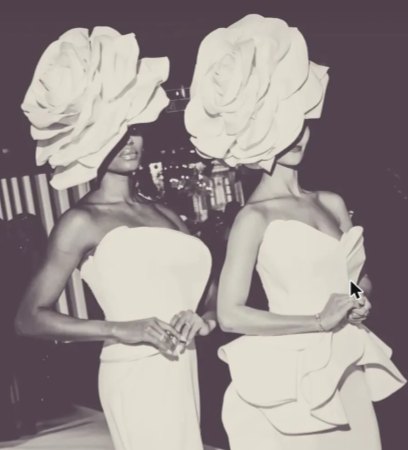 Dos performers con vestidos blancos y tocados de rosa gigante